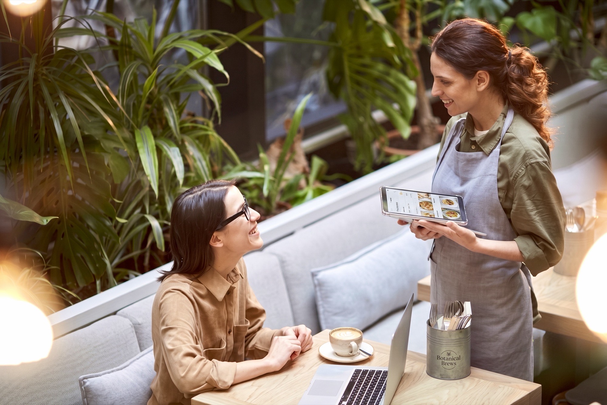A floor manager with a tablet talking with a guest at her table